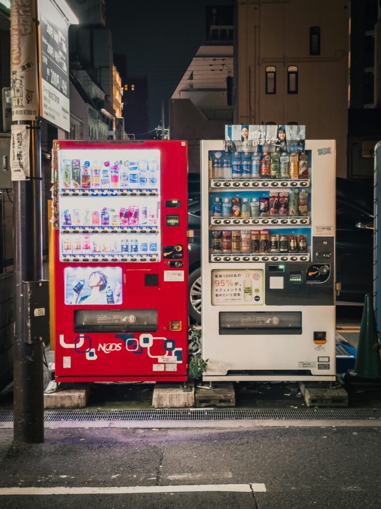 Colorful vending machines on an urban street in Osaka, Japan, illuminated at night.